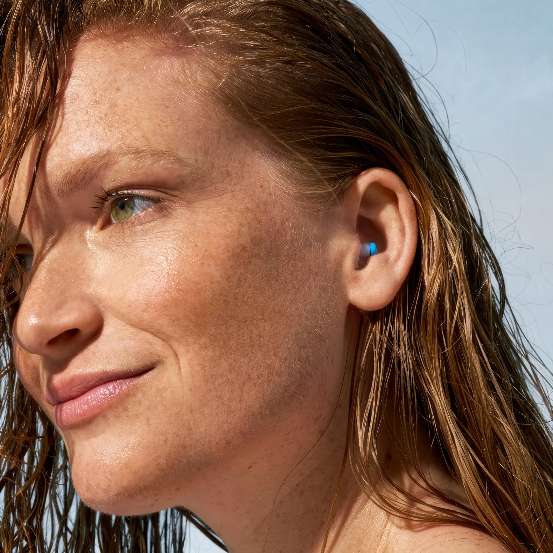Woman with wet hair wearing an Alpine SwimSafe earplug