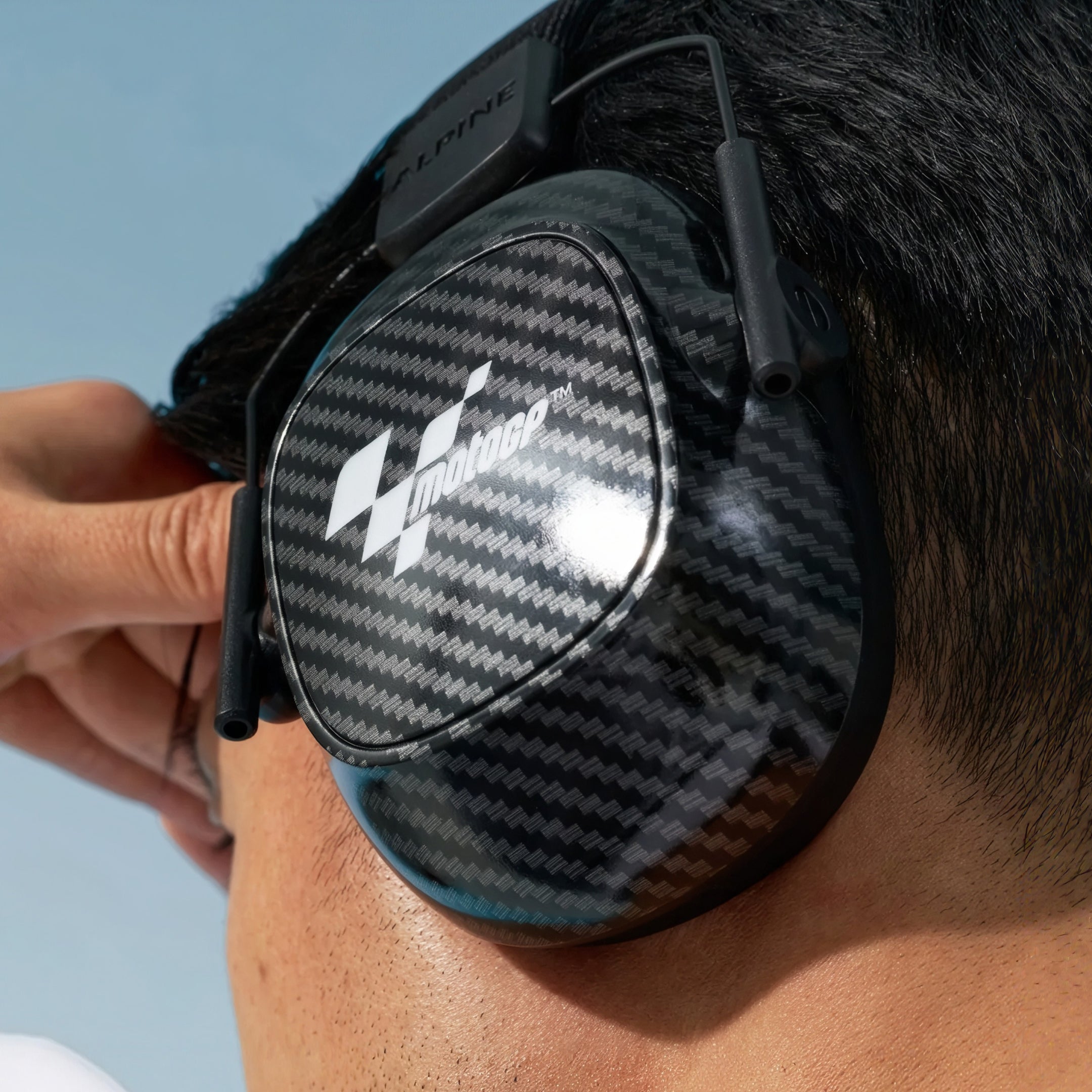 Man adjusting Alpine MotoGP Earmuffs on his head, seen from behind 